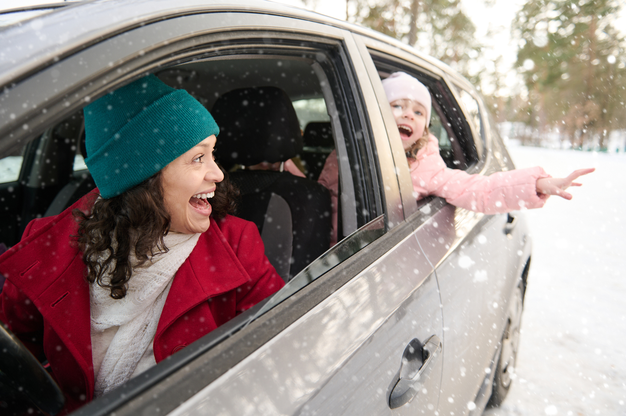 Happy family, mother and daughter in warm clothes travel by car on a beautiful cold snowy day. Adorable cheerful child, little girl catching snowflakes falling on her hand. Enjoy winter holiday