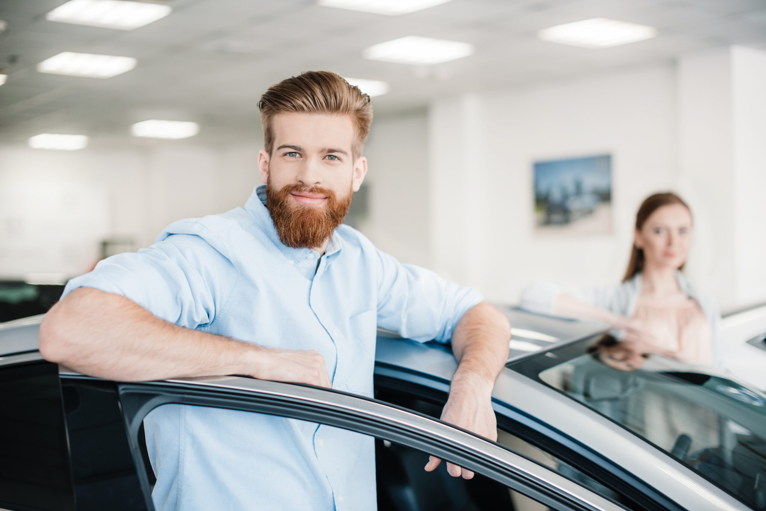happy-couple-standing-at-car-in-dealership-salon